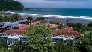 A coastal town with buildings overlooking a beach and ocean. - Lpb-2d (Jacó)
