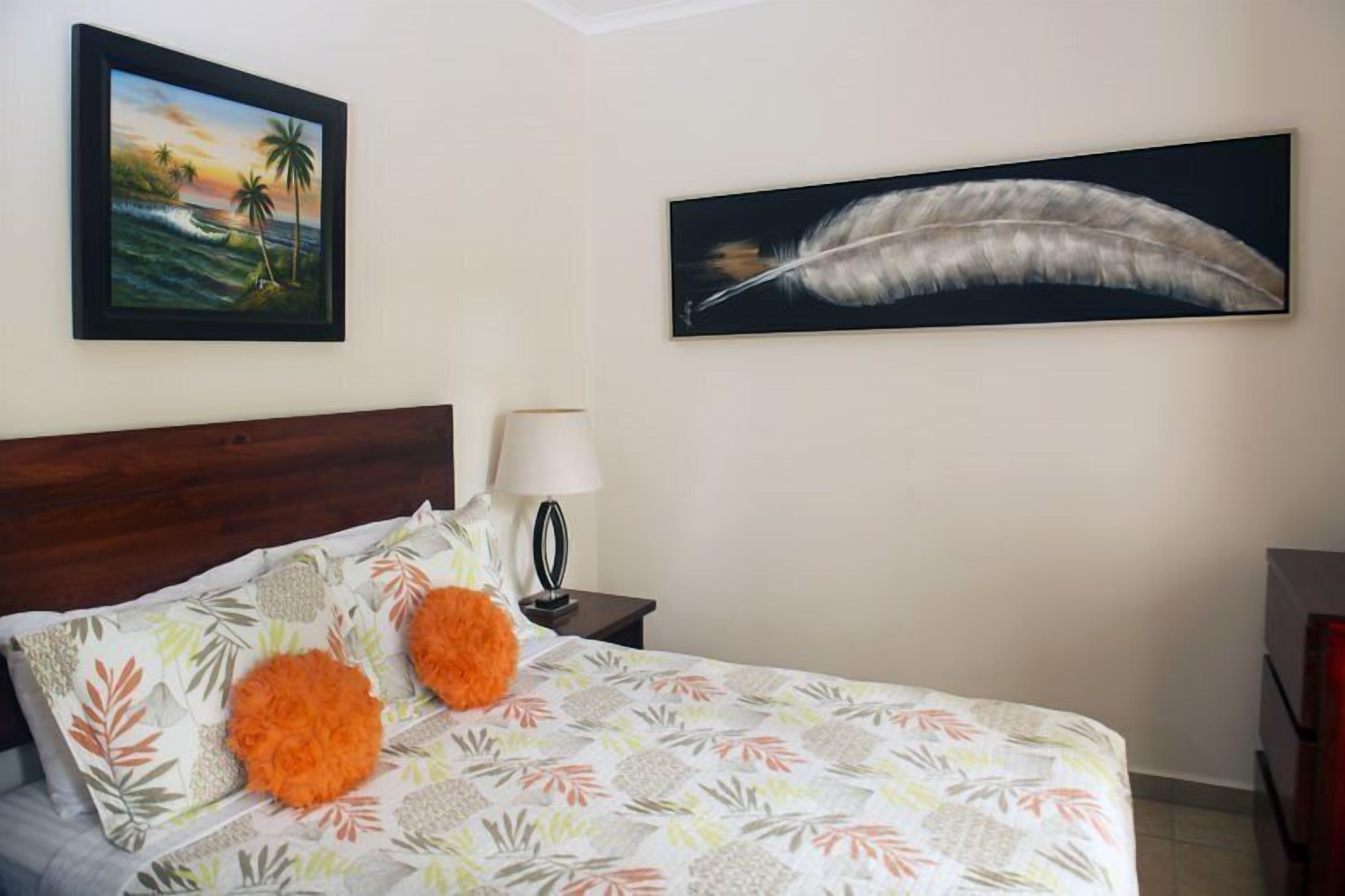 A bedroom with a bed, a nightstand, a lamp, and two wall-mounted paintings.