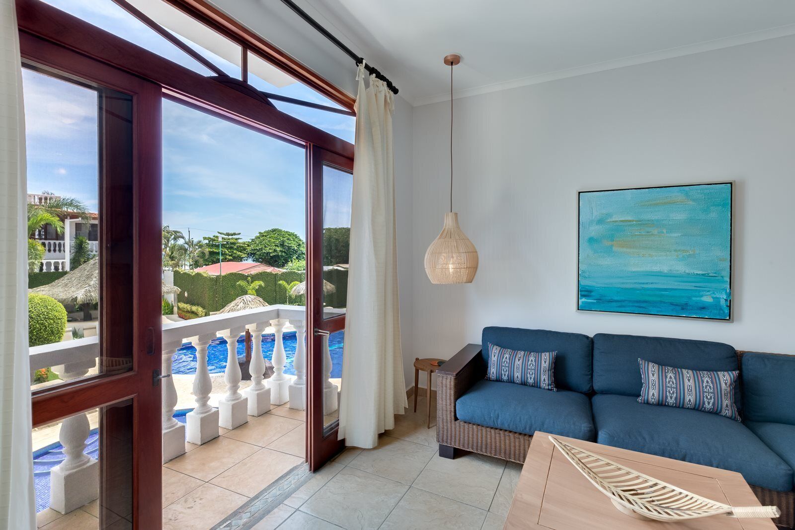 Salón con sofá azul, un cuadro y vistas a una piscina y follaje exterior.
