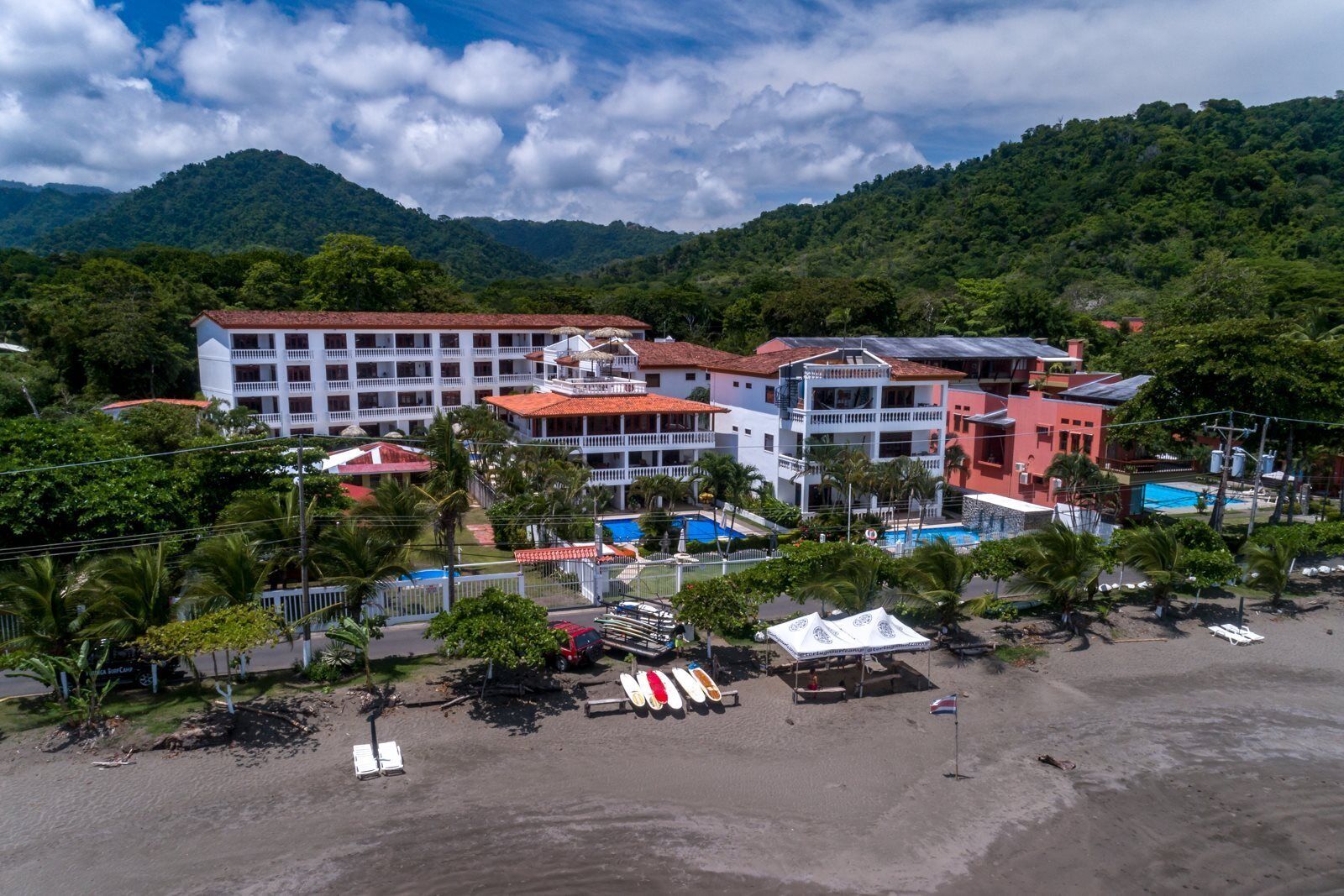 A hotel with multiple buildings, a beach, and mountains in the background.