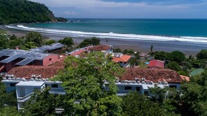 A coastal town with buildings overlooking a beach and ocean. - Lpb-2h (Jacó)