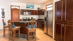 A kitchen with dark wooden cabinets, a stainless steel refrigerator, and a central island with chairs. - Lpb-2h (Jacó)