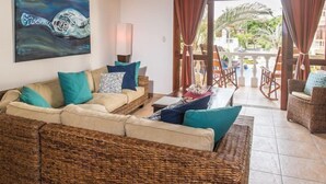 A living area with wicker furniture, a painting, and a view of an outdoor pool area. - Lpb-2h (Jacó)
