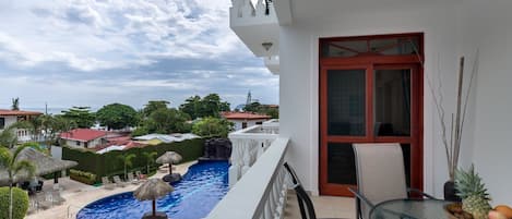 A balcony with a view of a swimming pool and surrounding greenery.