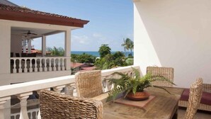 A balcony with wicker furniture, a potted plant, and a view of the ocean. - Lpb-3f (Jacó)