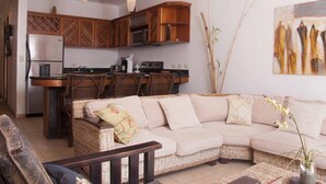 A living room with a sofa, a dining table, and a kitchen area with wooden cabinets and a refrigerator. - Lpb-3f (Jacó)