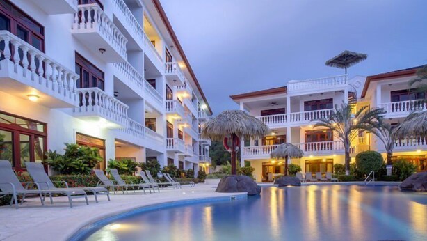 A hotel with multiple balconies, a swimming pool, and lounge chairs. - Lpb-4e (Jacó)