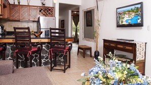 A dining area with a stone wall, wooden chairs, a table, and a television on the wall. - Lpb-4e (Jacó)