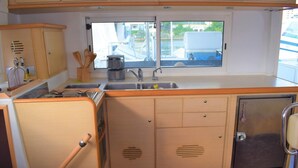 A compact kitchen with a sink, wooden cabinets, and a window overlooking a dock. - Catamaran Lagoon by Veleros Colombia (Cartagena)