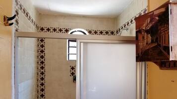 Un baño con cabina de ducha, inodoro y un pequeño estante con un objeto decorativo.