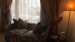 A living room with a patterned sofa, a lamp, and a view of buildings through sheer curtains. - Apart Hotel Dos Providencia (Santiago)