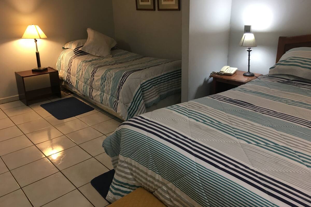 A hotel room with two beds, a nightstand with a lamp, a phone, and framed pictures on the wall.