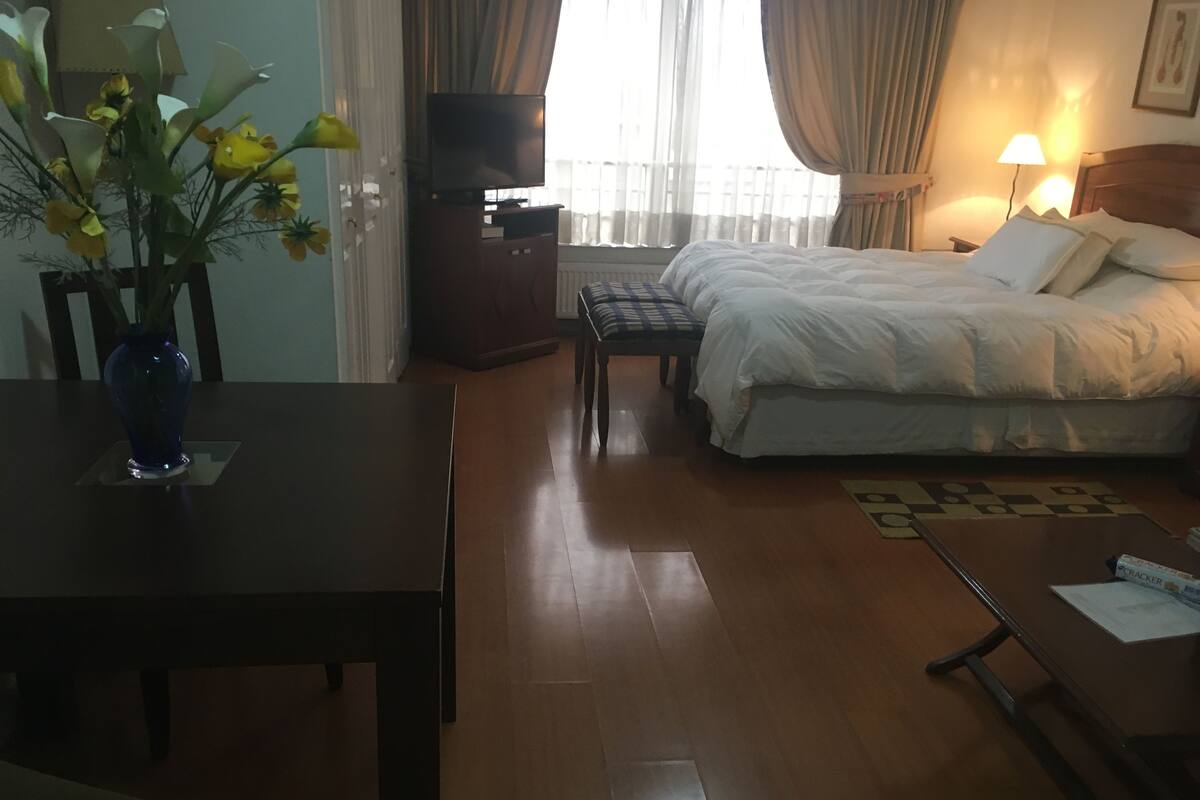 A hotel room with a bed, a TV, a desk, and a vase of flowers.