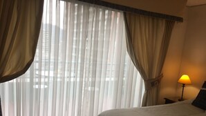 A hotel room with a bed, a nightstand with a lamp, and sheer curtains. - Apart Hotel Dos Providencia (Santiago)