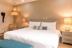 A bedroom with a large bed, two bedside tables, a chair, and a hanging lamp.