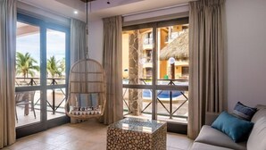 Une pièce dotée d’un fauteuil suspendu, d’un canapé confortable, d’une table basse en verre et de grandes fenêtres donnant sur une piscine et des palmiers.