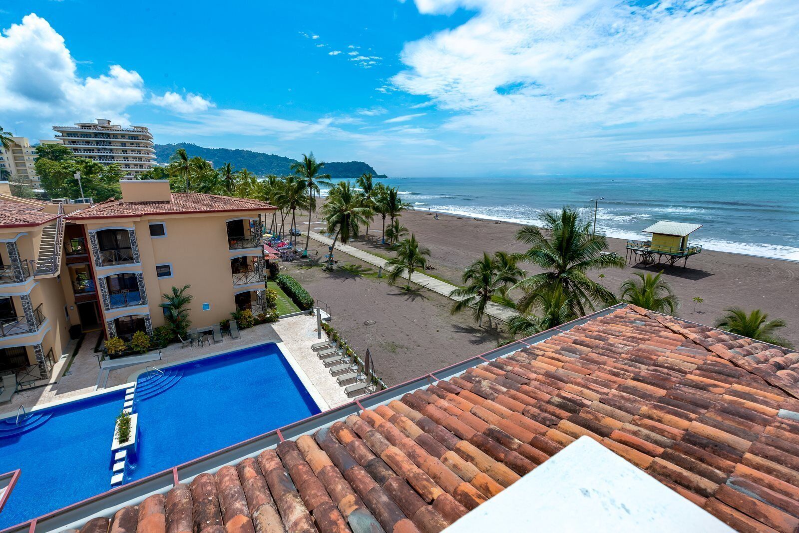 A hotel with a swimming pool, beach view, and palm trees.