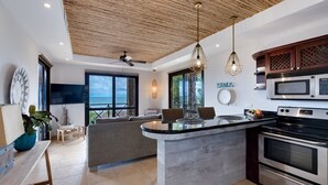 A modern kitchen with a central island, built-in oven, and microwave. There is a seating area with a view of the ocean. - Oceanfront Penthouse / Upscale Roof Terrace (Jacó)
