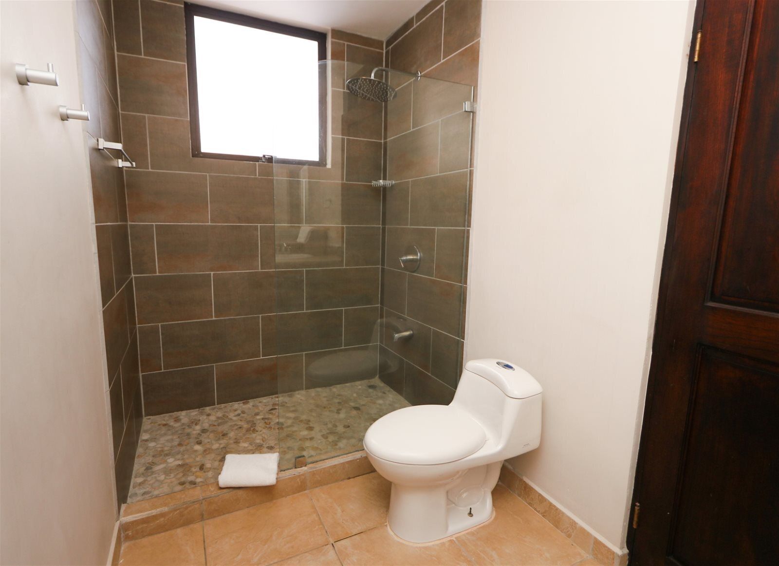 Een kleine badkamer met douche, toilet en een raam.