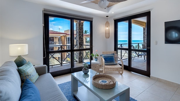 A modern living room with a sofa, a coffee table, and a wicker chair. Large glass doors lead to an outdoor patio with a view of the ocean. - Amazing Seaside Penthouse With Rooftop Terrace (Jacó)
