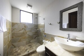 A bathroom with a stone shower, a white sink, and a large mirror.