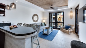 A modern kitchen with a curved island, a dining area with wicker furniture, and a living space with a sofa and a TV. - Amazing Seaside Penthouse With Rooftop Terrace (Jacó)