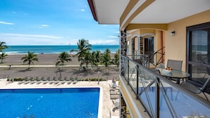 A balcony with a pool, overlooking a beach with palm trees and a clear blue sky. - Amazing Seaside Penthouse With Rooftop Terrace (Jacó)