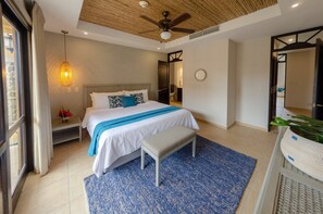 A modern hotel room with a large bed, a bench, a ceiling fan, and a large window.