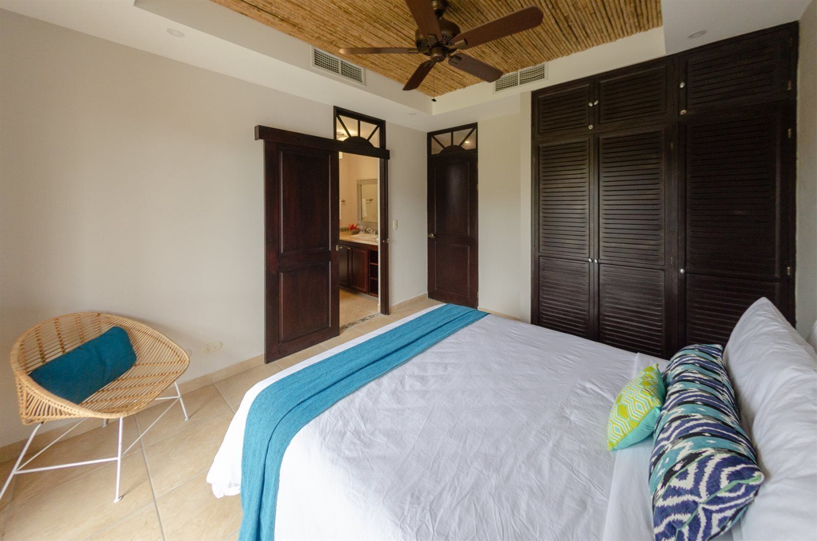 A bedroom with a bed, a wicker chair, a ceiling fan, and a wardrobe.