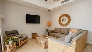 Uma sala de estar com sofá, duas poltronas, uma mesa de centro e televisão fixada na parede.