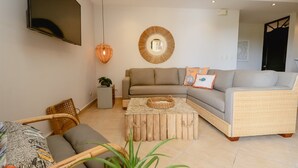 Uma sala de estar moderna com um sofá seccional, uma mesa de centro, uma TV fixada na parede e uma poltrona de vime.