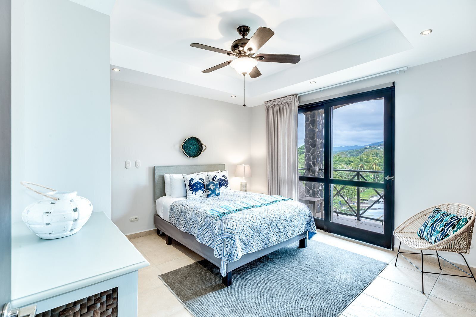 Ein modernes Schlafzimmer mit einem Bett, einem Deckenventilator, einem großen Fenster und Blick ins Freie.