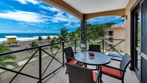 A balcony with a table and chairs, overlooking a beach with palm trees and a view of the ocean. - Be-3l (Jacó)