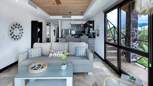 A modern living room with a sofa, coffee table, and a view of the kitchen and outdoor area. - Be-3l (Jacó)