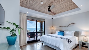A modern bedroom with a large bed, a ceiling fan, a potted plant, and a view of the ocean through a glass door. - Be-3l (Jacó)