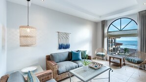 Ein modernes Wohnzimmer mit einer Couch, einem Couchtisch und Korbstühlen. Ein großes Fenster bietet Blick auf den Ozean.