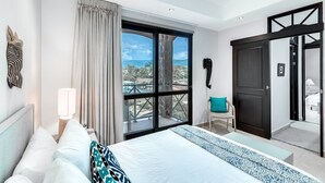 Ein Hotelzimmer mit Bett, Sessel, Schreibtisch, Lampe, großem Fenster mit Aussicht und einer Tür.