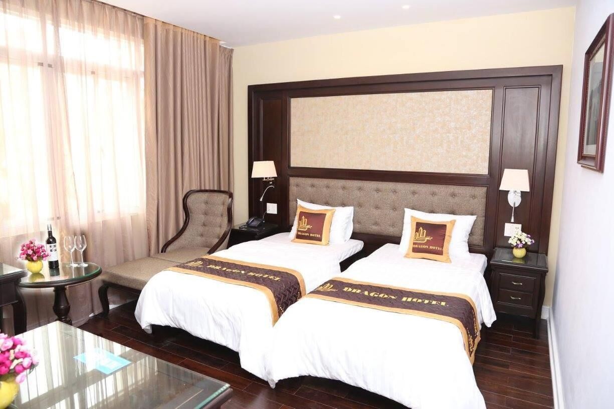 Une chambre d’hôtel avec deux lits, un coin salon, une petite table ornée d’un vase de fleurs et une lampe.