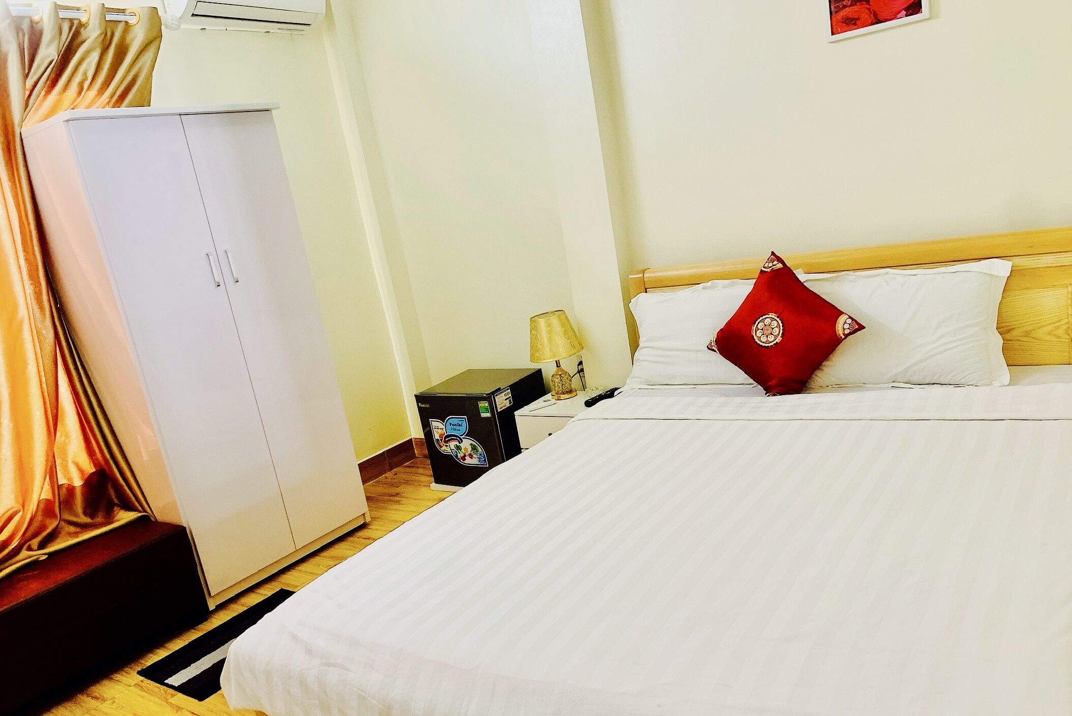 A hotel room with a bed, a wardrobe, a desk with a lamp, and a refrigerator.