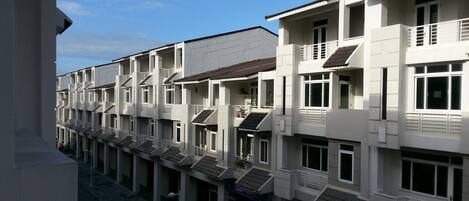 A row of white buildings with balconies, a clear sky, and a paved ground.