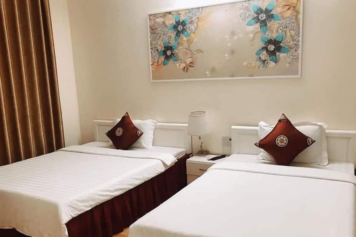 A hotel room with two beds, a nightstand, a lamp, and a floral artwork on the wall.