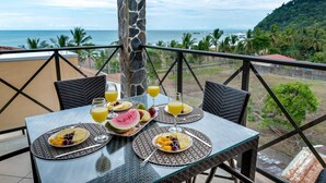A table set with breakfast items and drinks on a balcony with a view of the ocean and hills. - 5th Flr Ocean View Penthouse With 2 Level Balcony (Jacó)