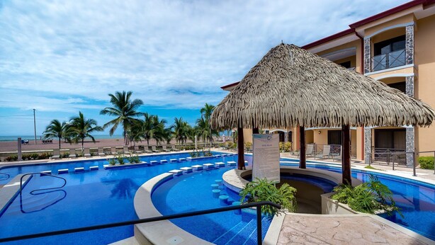 A pool area with a thatched roof structure, palm trees, and a view of the beach. - 5th Flr Ocean View Penthouse With 2 Level Balcony (Jacó)