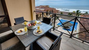 A balcony with a table set for breakfast, overlooking a pool and ocean view. - Perfect Oceanfront Retreat for Your Family (Jacó)