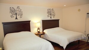 A hotel room with two single beds, a nightstand with a lamp, and wall decorations of trees. - Stanford House (Manchester Center)