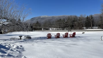A snowy landscape with four red Adirondack chairs lined up facing a sign that reads "Nippert Cafe."