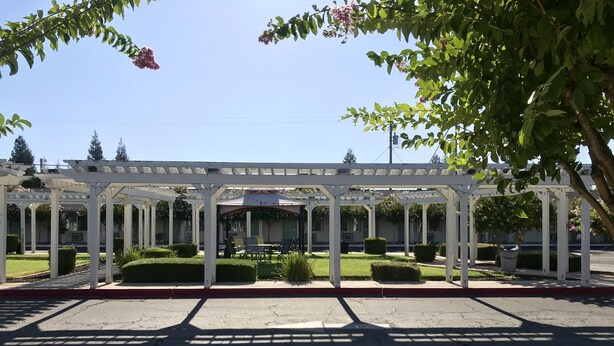 A covered outdoor seating area with white columns, surrounded by greenery and a clear sky. - Sunrise Inn Turlock (Turlock)