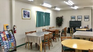 A dining area with multiple tables and chairs, a fire extinguisher, framed pictures on the wall, and a television. - Sunrise Inn Turlock (Turlock)
