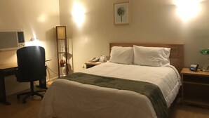 A hotel room with a bed, a desk with a chair, a nightstand with a lamp, and a wall-mounted air conditioner. - Sunrise Inn Turlock (Turlock)