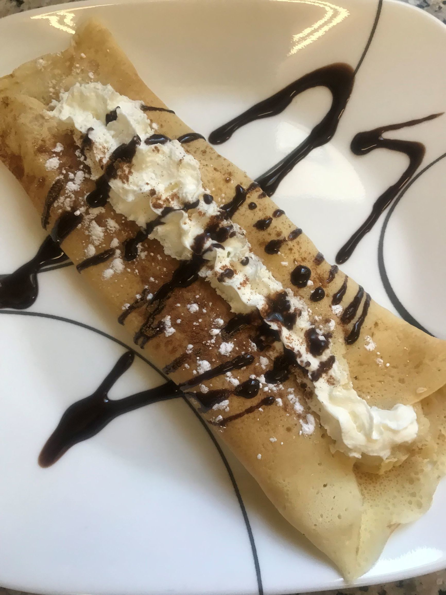 Une crêpe garnie de crème fouettée et nappée de chocolat, présentée sur une assiette.